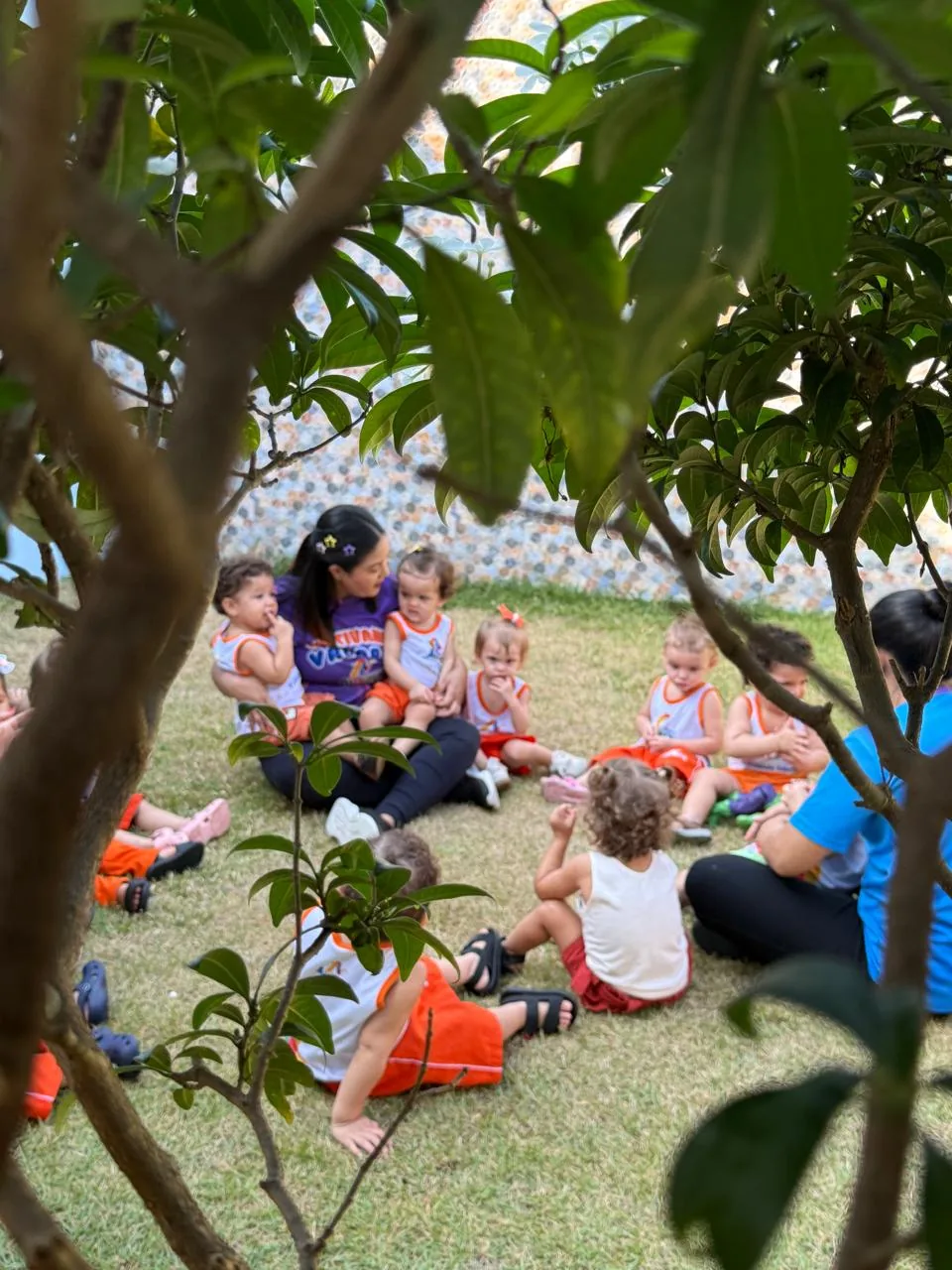 Crianças com educadoras sentadas em roda ao ar livre